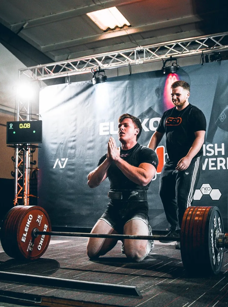Mike kneeling behind a loaded deadlift bar on a competition platform