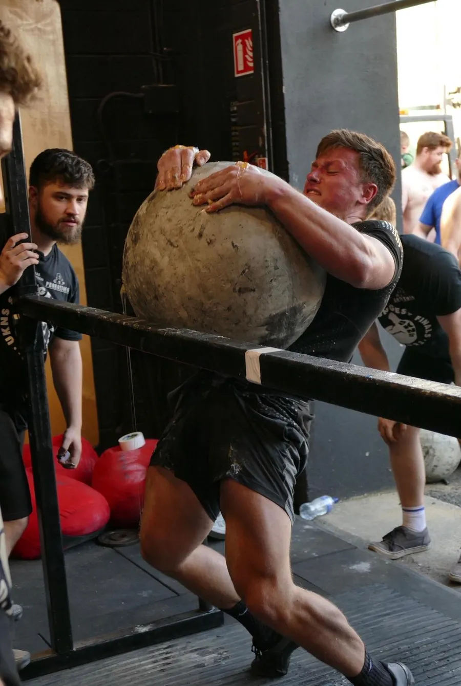 Mike loading an atlas stone over a bar at a strongman competition